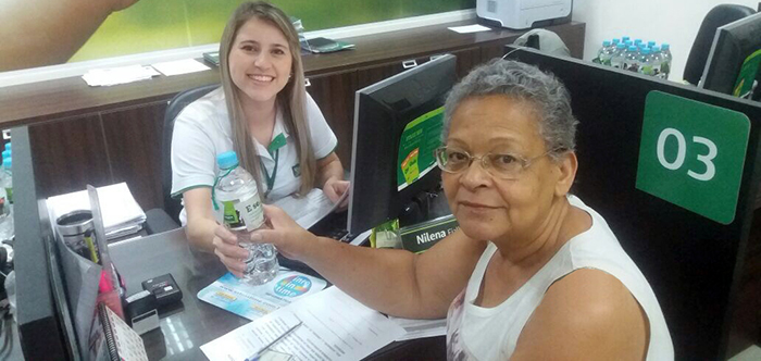 Colaboradora posa para foto entregando garrafa de água personalizada em prol da campanha Mude 1 Hábito.