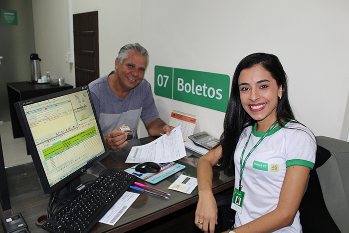 Cliente recebendo o brownie como lembrança pelos 45 anos e a colaboradora de Atendimento, Leticia de Oliveira, vestindo a camisa comemorativa 