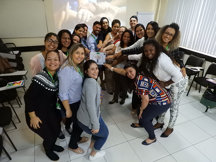 Colaboradores com a placa do setor ilustrando a fusão das áreas