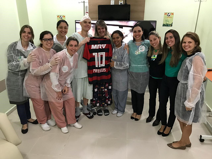 Matheus, acompanhado de sua mãe e a equipe interna do hospital no momento em que foi surpreendido com a entrega da blusa personalizada do seu time e a TV preparada no quarto.